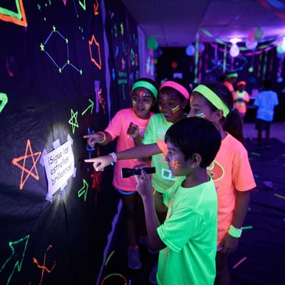 Niños con linterna siguiendo pistas fluorescentes en la búsqueda del tesoro nocturna de Glow Night Party