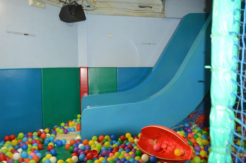 Piscina de bolas con tobogán azul y paneles acolchados en otra sala de FlipoPark
