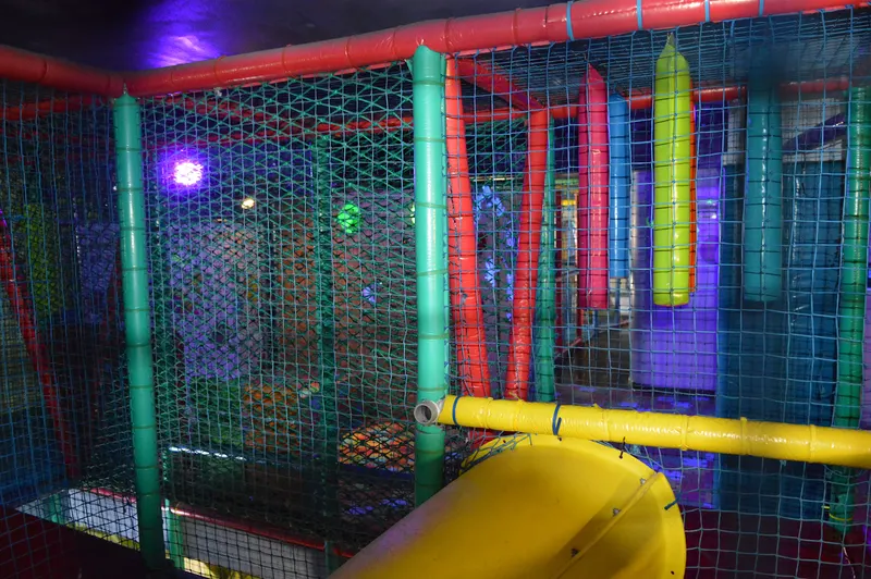 Pasillo de red con columnas de espuma de colores colgando en una zona de juego en penumbra