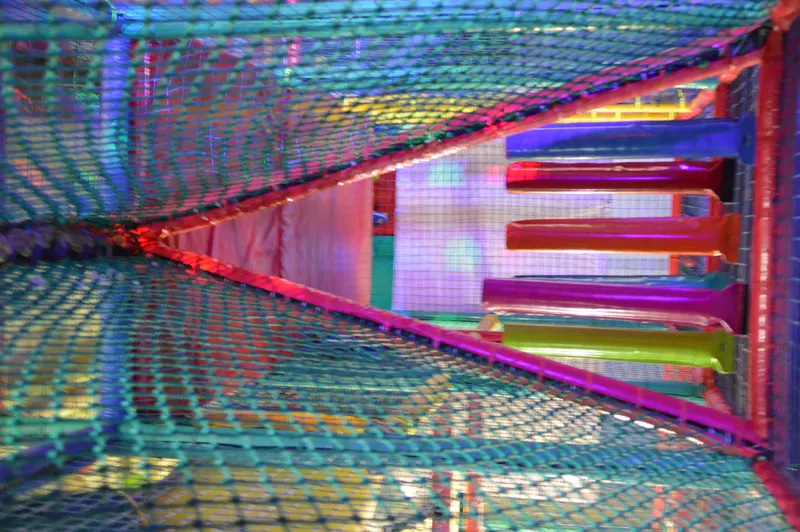 Vista interior de un túnel de red iluminado con tubos de colores en la estructura de juego