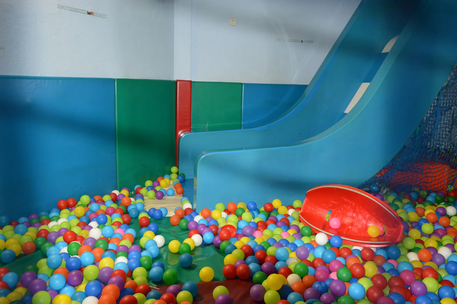 Tobogán azul que desemboca en la piscina de bolas de colores de FlipoPark, con red de túneles al fondo